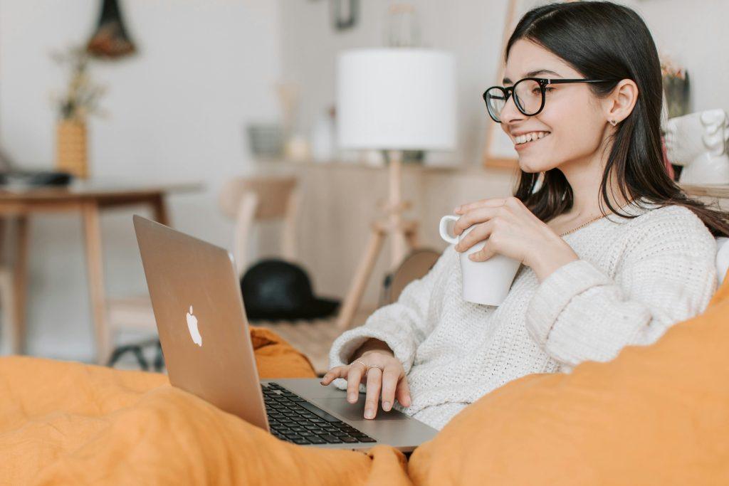Chica tomando un café mientras mira su ordenador feliz.