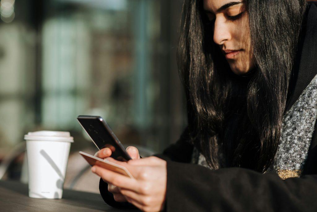 Una mujer mirando precios de máquinas de café para su empresa en su teléfono móvil.