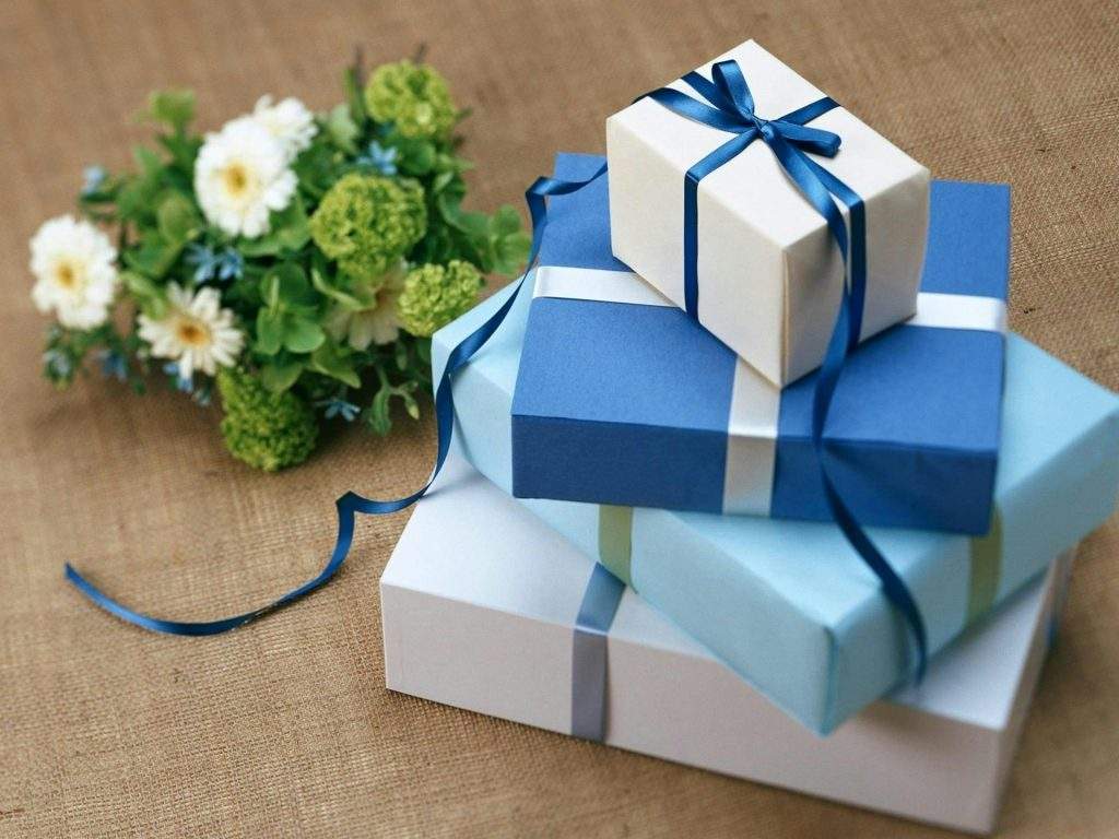 Un conjunto de regalos de color azul y blanco, al lado de unas flores.