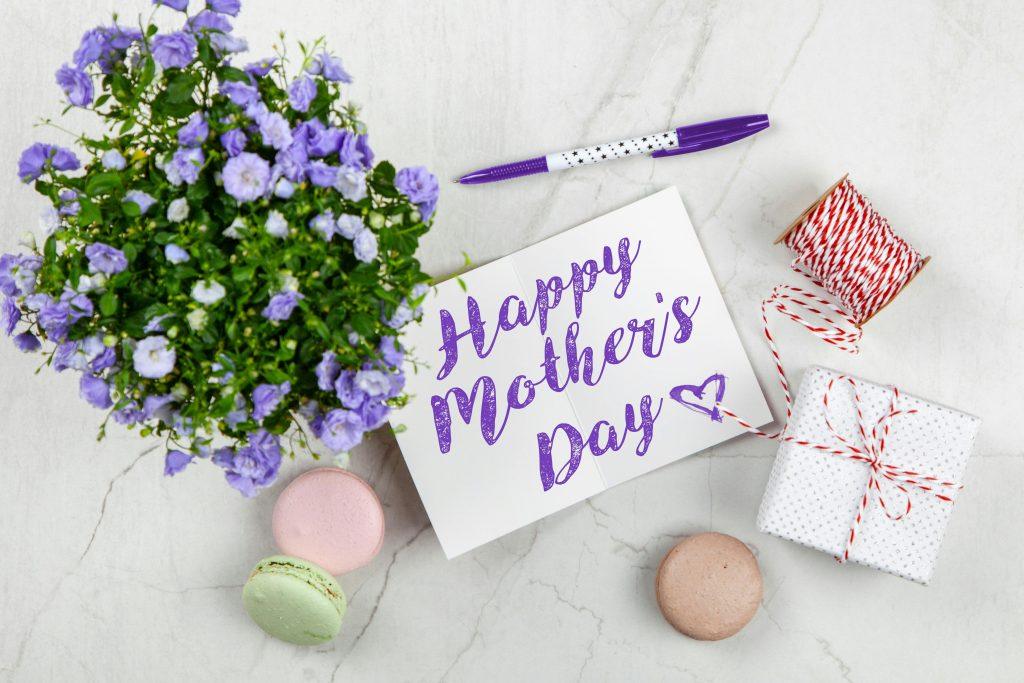Un ramo de rosas moradas, con una carta que felicita a una futura mama, con regalos a su alrededor