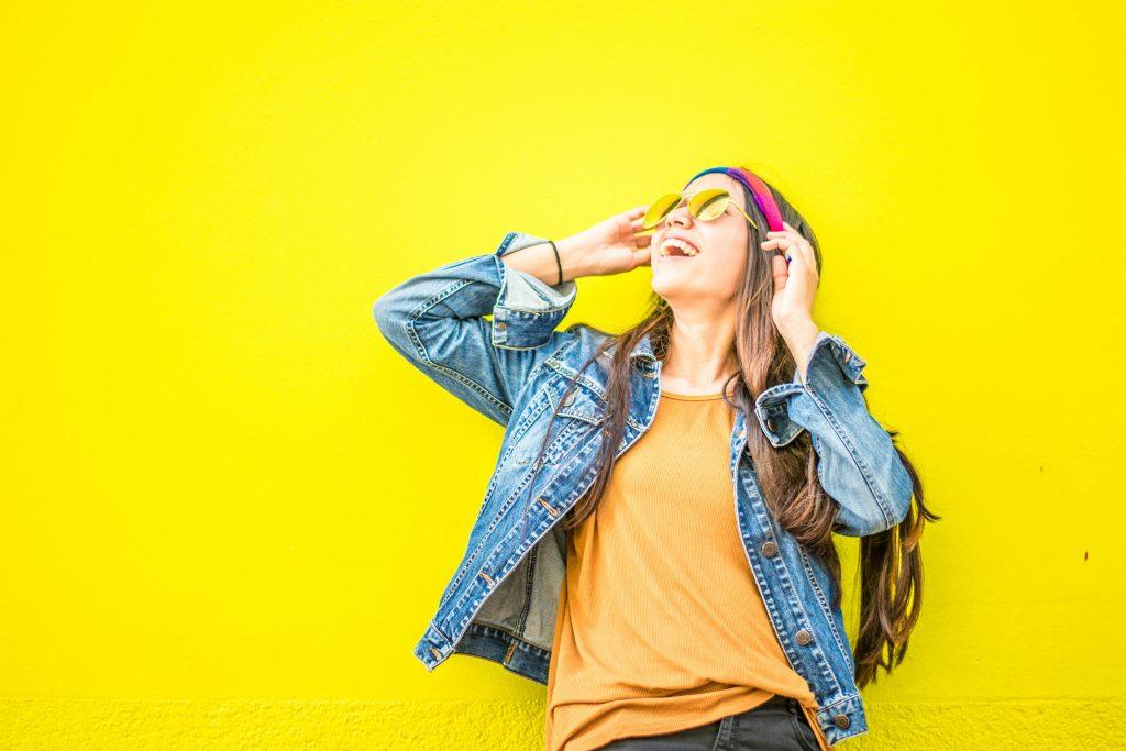 Una mujer escuchando música, con unos cascos rosas en un fondo amarillo.