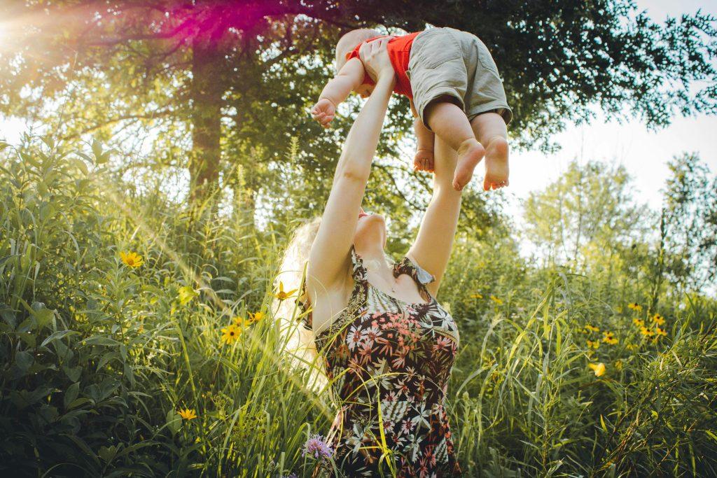 Una futura mama aupando a su hijo en un bosque.