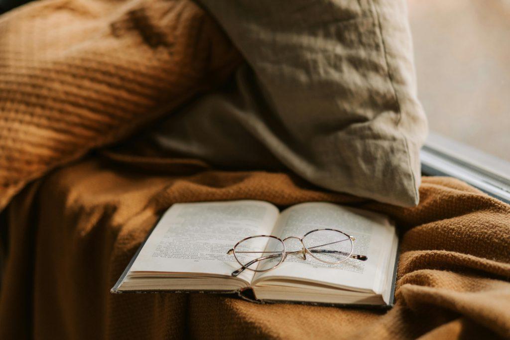 Un libro acostado en un sofa con unas gafas y un libro.