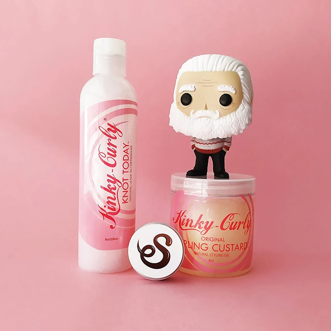 Un funko pop encima de dos productos de Kinky curly en un fondo rosado