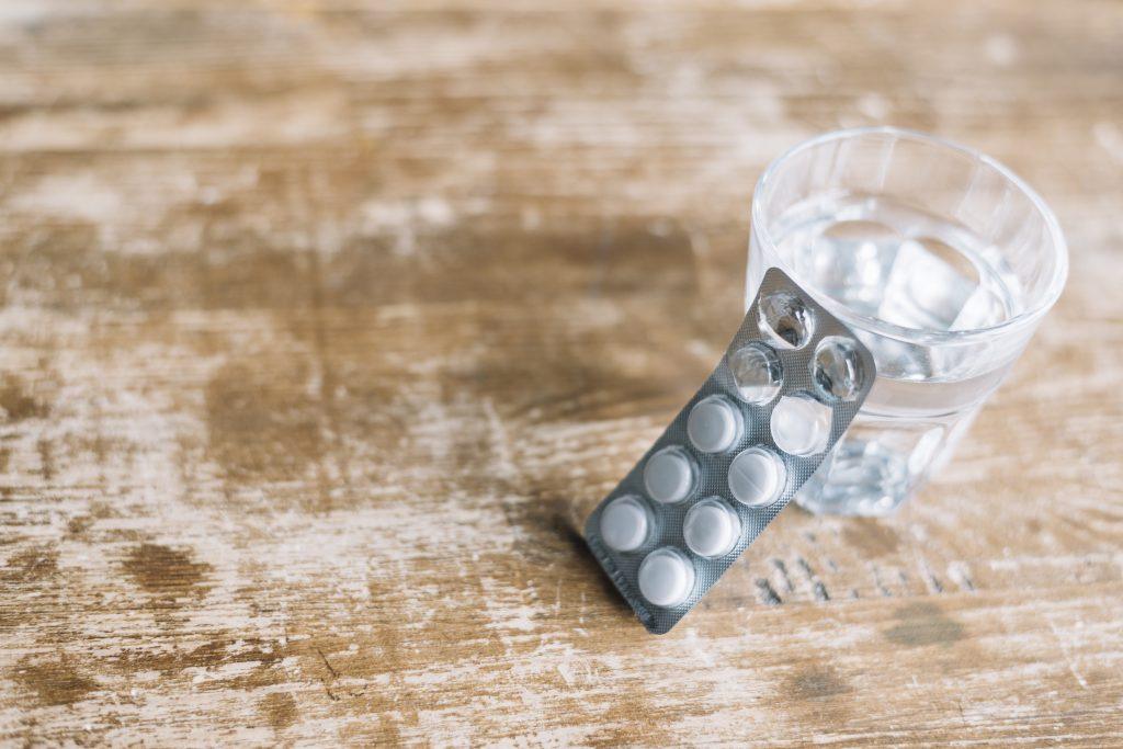 Una imagen de las mejores pastillas para la caída del cabello en mujeres al lado de un vaso de agua