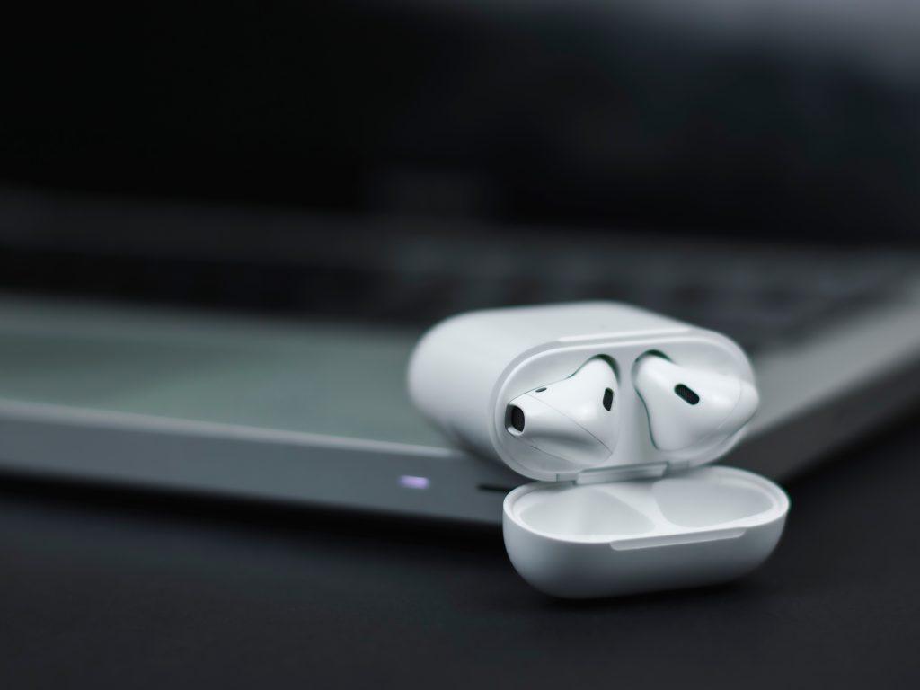 Unos cascos de móvil blancos apoyados en una mesa de la marca Mac.