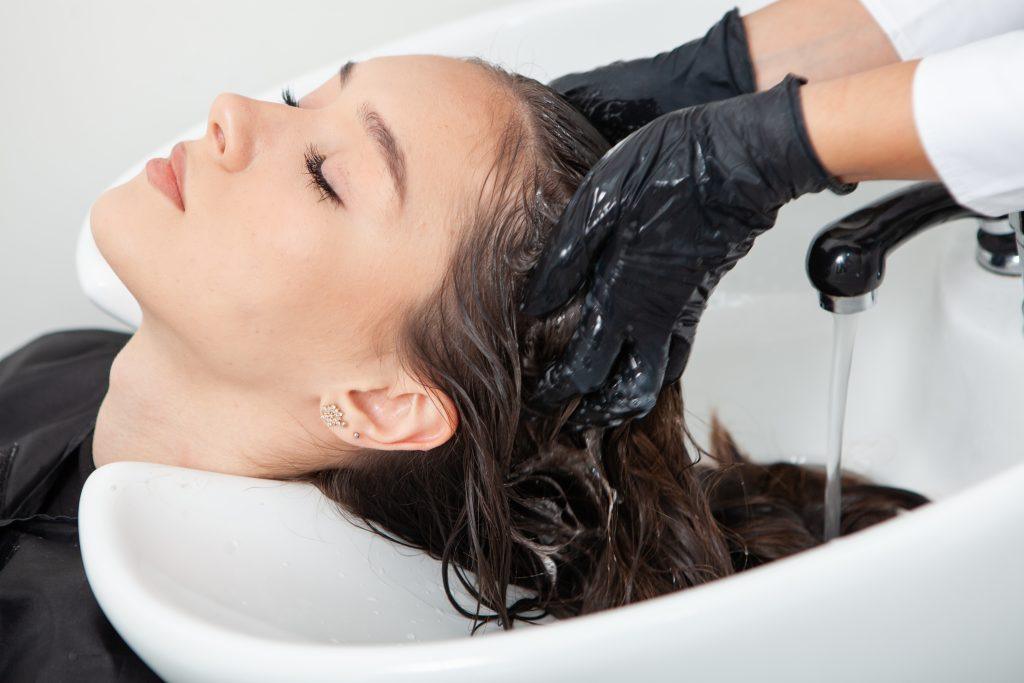 Una mujer en una peluquería relajada, aplicando en su pelo pastillas para la caída del cabello.