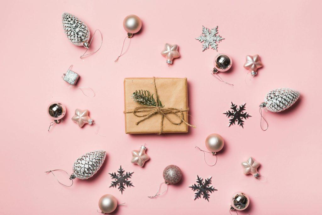 Una imagen de un regalo con decoración de navidad al rededor con el fondo rosado