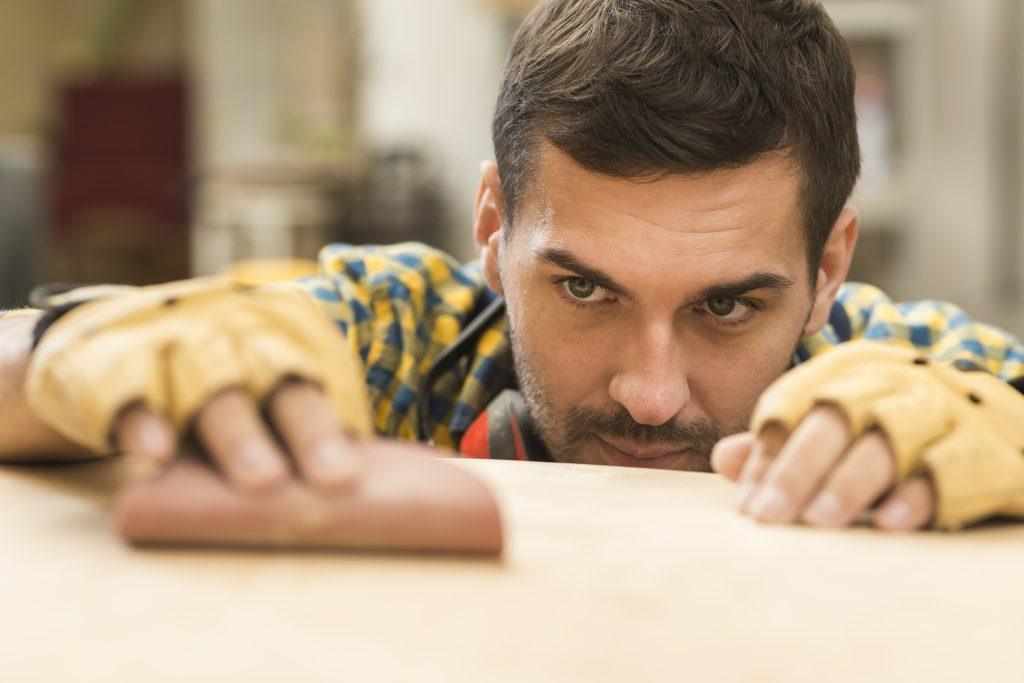 Un hombre lijando madera, con una herramienta profesional