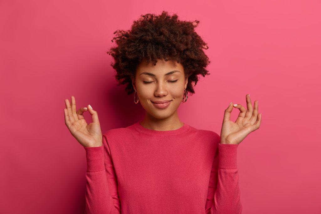 Una chica de color meditando con un fondo rosado