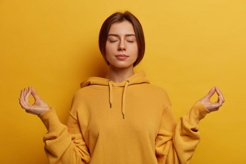 Una chica meditando con un fondo de color naranja esperando que las frases de karma surtan su efecto a gente que se cree buena